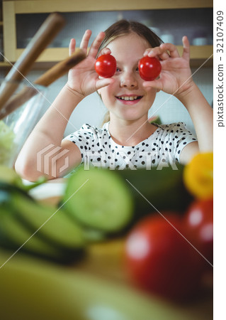 Playful girl holding cherry tomato on her eye Playful girl holding cherry tomato on her eye 32107409