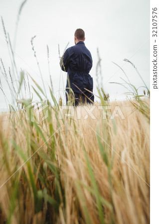 Rear view farmer standing with arms crossed in the field 32107576