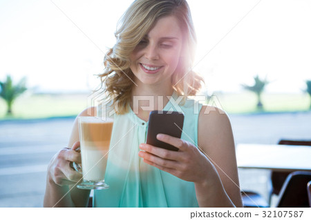 Smiling woman holding a coffee glass and using her mobile phone Smiling woman holding a coffee glass and using her mobile phone 32107587