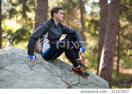 Male biker relaxing on rock in forest Male biker relaxing on rock in forest 32107857