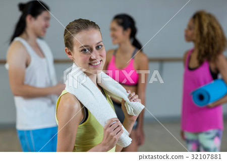 Portrait of female trainer holding towel with fitness class in background Portrait of female trainer holding towel with fitness class in background 32107881