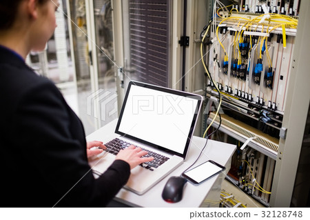 Technician using laptop while analyzing server Technician using laptop while analyzing server 32128748