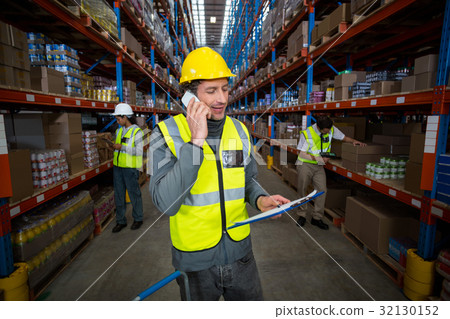 Warehouse worker talking on mobile phone and holding clipboard Warehouse worker talking on mobile phone and holding clipboard 32130152