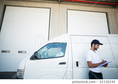Delivery man writing on clipboard while standing next to his van Delivery man writing on clipboard while standing next to his van 32130248