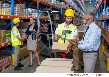 Warehouse manager holding digital tablet while male worker scanning barcode 32130406