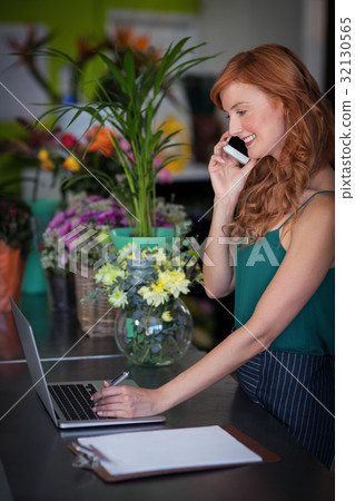 Female florist talking on mobile phone while using laptop 32130565