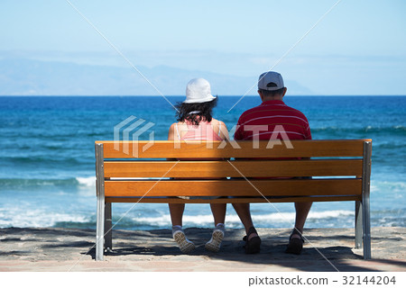 Seniors couple sitting on bench at the beach 32144204