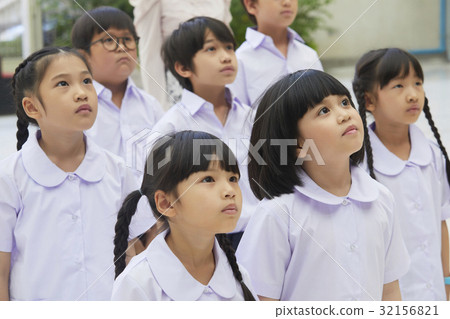 Boys and girls in uniform are standing and looking at something. 32156821