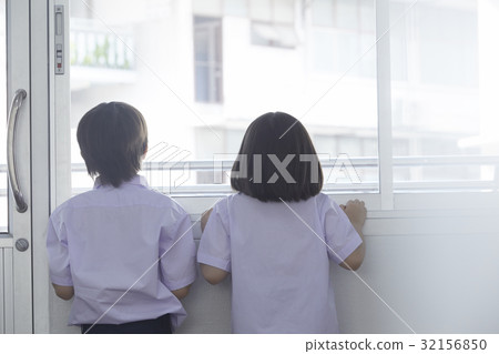 A schoolboy and a schoolgirl are standing near window and looking at outside 32156850