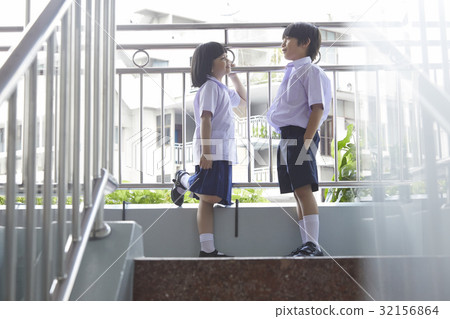 A schoolboy and a schoolgirl are standing on stairs and talking happily. 32156864