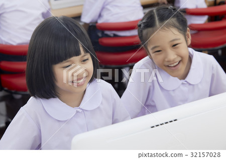 Two schoolgirls are smiling, looking and using the computer in class 32157028