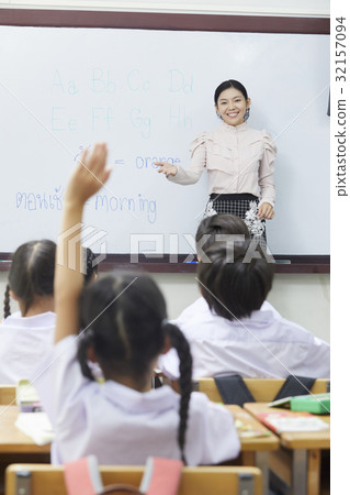 a teacher is inviting a girl raising her hand to answer in English class. 32157094