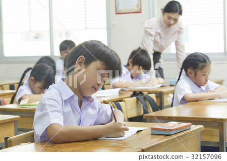 pupils are writing and a teacher is looking at one of them. pupils are writing and a teacher is looking at one of them. 32157096