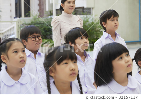 teacher and students are standing outside and staring at something. 32157117