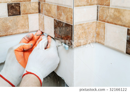 The tiler's hands are using plastic wedges. 32166122