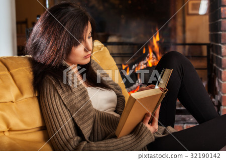 Woman reading a book by fireplace 32190142