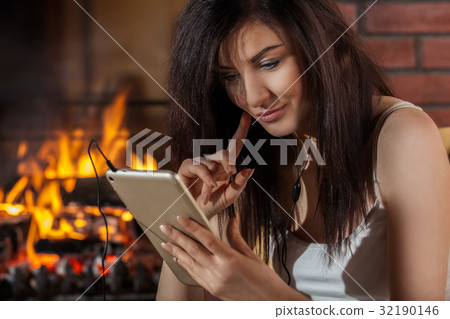 Woman using digital tablet sitting by fireplace 32190146