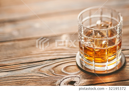 Glass of whiskey with ice cubes on wooden table Glass of whiskey with ice cubes on wooden table 32195372