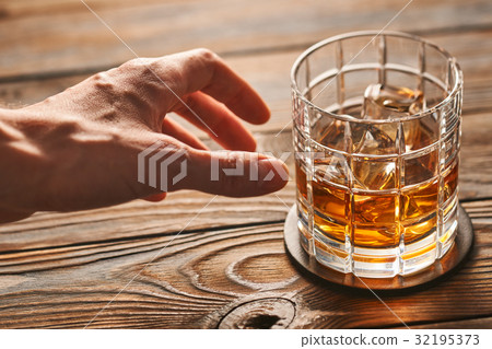 Man's hand reaching to glass of whiskey Man's hand reaching to glass of whiskey 32195373
