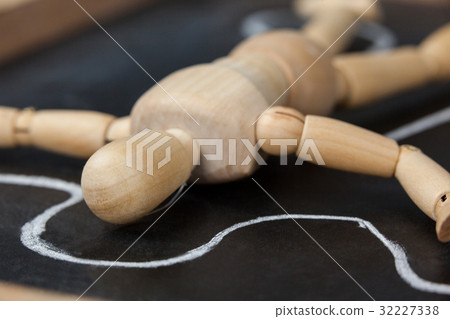 Wooden figurine lying on a slate board with border around his body Wooden figurine lying on a slate board with border around his body 32227338