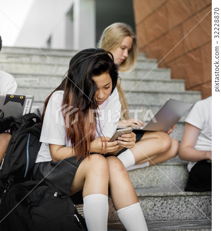 Group of students sitting at stairs and using digital devices Group of students sitting at stairs and using digital devices 32228870