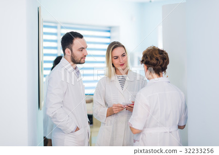 Mature doctor discussing with nurses in a hallway Mature doctor discussing with nurses in a hallway 32233256