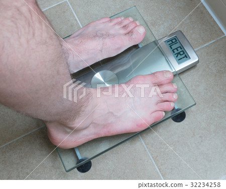 Man's feet on weight scale - Alert 32234258