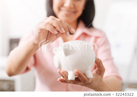 Positive woman putting coins into a piggy bank Positive woman putting coins into a piggy bank 32243322
