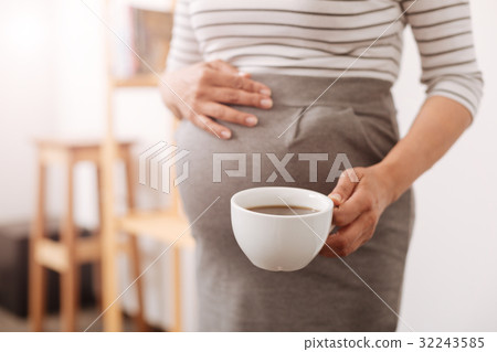 Pleasant pregnant woman holding a cup of coffee Pleasant pregnant woman holding a cup of coffee 32243585