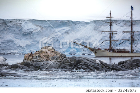 A large ship stands behind stones with penguin.And 32248672