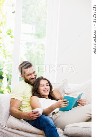 Man holding a cup of coffee while woman reading book 32255235