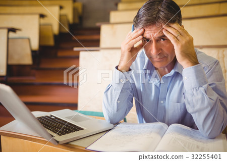 Depressed professor sitting with notes and laptop Depressed professor sitting with notes and laptop 32255401