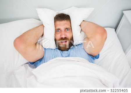 Man covering ears with pillow in bed 32255405