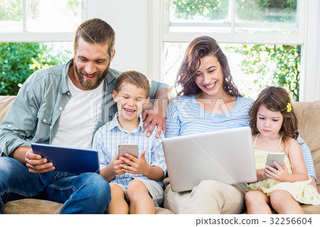 Family sitting on sofa and using a laptop, tablet and phone 32256604