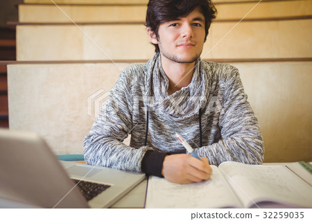 Portrait of young student sitting on desk reading notes 32259035