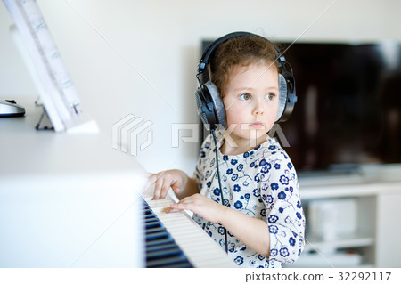 Beautiful little kid girl playing piano in living Beautiful little kid girl playing piano in living 32292117
