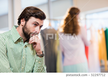 Bored man waiting his wife while woman by clothes rack 32297712