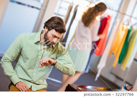 Bored man waiting his wife while woman by clothes rack 32297766