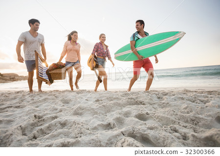 Friends carrying a surfboard and basket Friends carrying a surfboard and basket 32300366