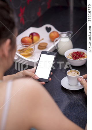Young woman having breakfast using smartphone 32316779