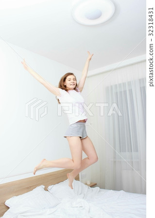 Portrait of a young happy woman jumping on bed 32318431