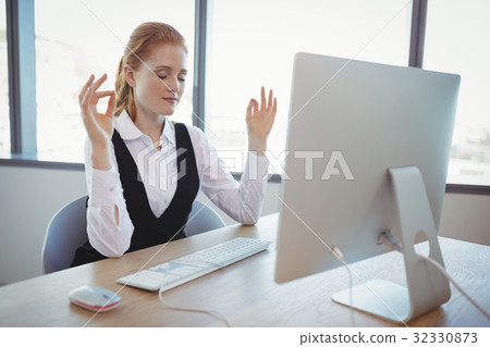 Beautiful executive performing yoga at desk 32330873