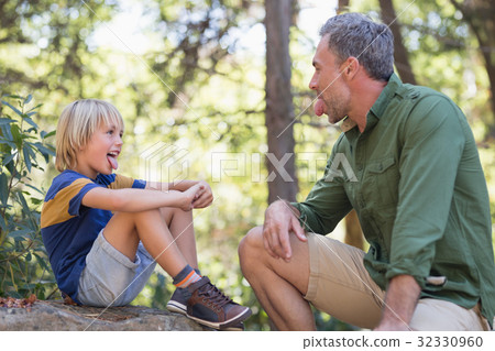 Father and son sticking out tongue while sitting in forest Father and son sticking out tongue while sitting in forest 32330960
