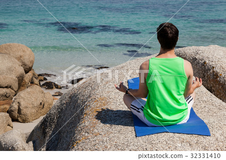 Man performing yoga on rock near the coast Man performing yoga on rock near the coast 32331410