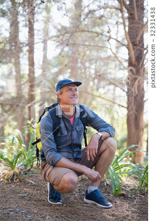 Happy hiker kneeling against trees 32331438