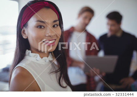 Smiling businesswoman standing with colleagues in background 32331444