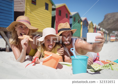 Happy family taking selfie while lying on blanket at beach Happy family taking selfie while lying on blanket at beach 32331651