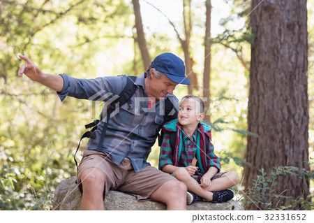 Father and son sitting on rock while pointing away Father and son sitting on rock while pointing away 32331652