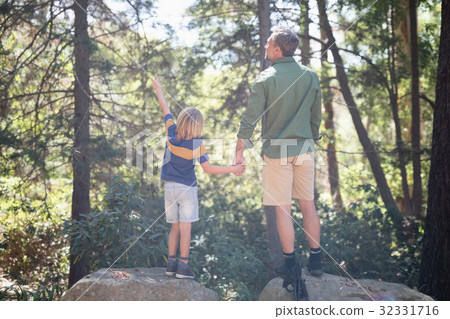 Boy pointing way while standing with father in forest 32331716