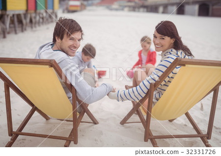 Portrait of parents relaxing on launge chairs with children playing in background 32331726